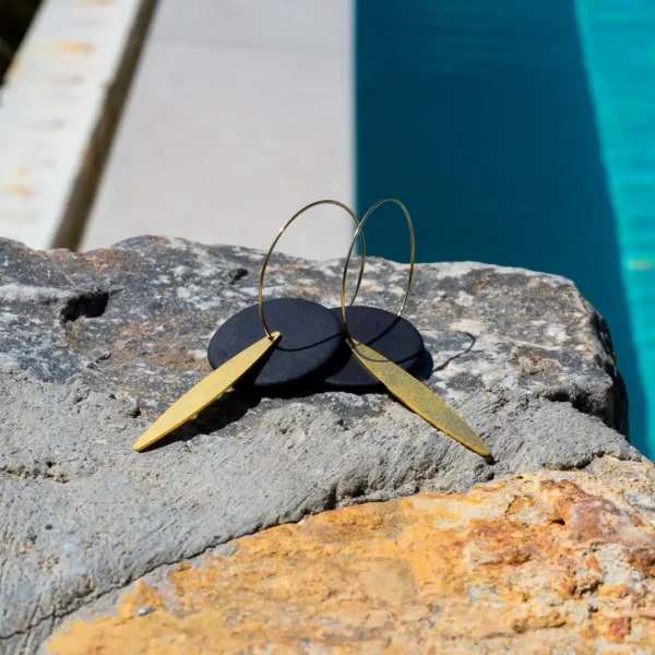 Créoles Eléa posées sur une pierre - disques de grès noir mat et feuilles en laiton dorées à l'or fin - des boucles d'oreilles artisanales par Photyne