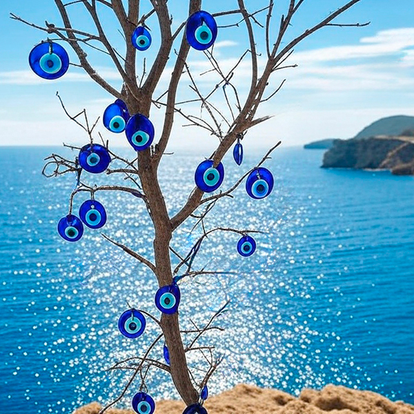 ensemble de breloques en verre au motif oeil bleu grec (Mati) suspendus aux branches d'un arbre mort, planté sur un rocher au bord de la Méditerranée