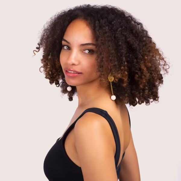 Élégantes boucles d’oreilles avec perles de lave blanche suspendues à une chaîne dorée.