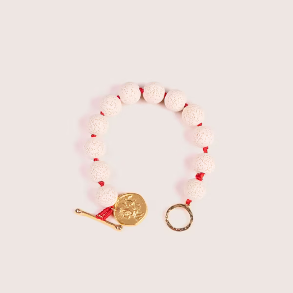 Accessoire tendance : bracelet Oia en pierre de lave blanche et médaille dorée.
