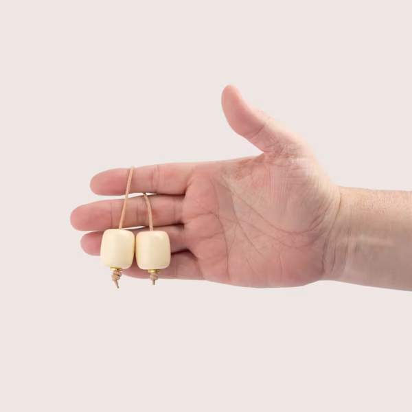 Main manipulant un bégleri de couleur crème - deux perles et un lacet de cuir brun -une création Photyne