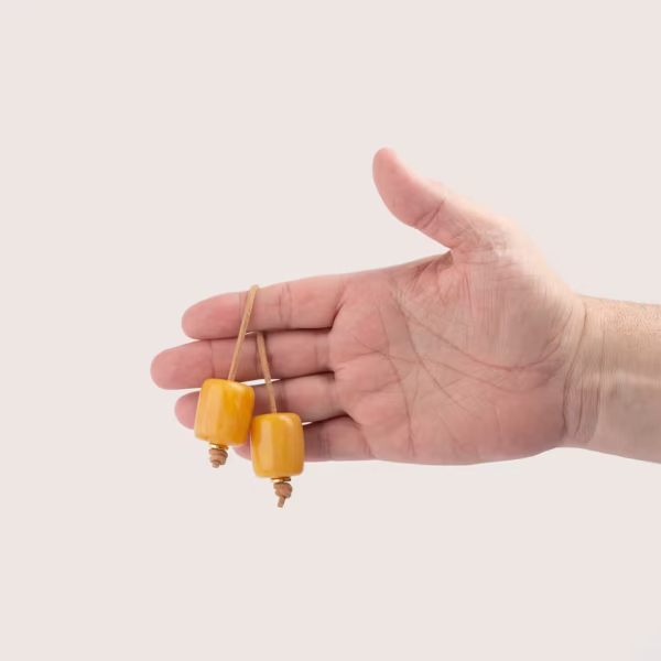 Main manipulant un bégleri de couleur ambre - deux perles et un lacet de cuir brun -une création Photyne