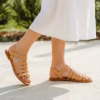 Sandales en cuir gladiateur portée par une jeune fille avec robe blanche longue qui marche sur des pavés ensoleillés - ambiance estivale méditerranéenne -modèle Chora- une création Photyne