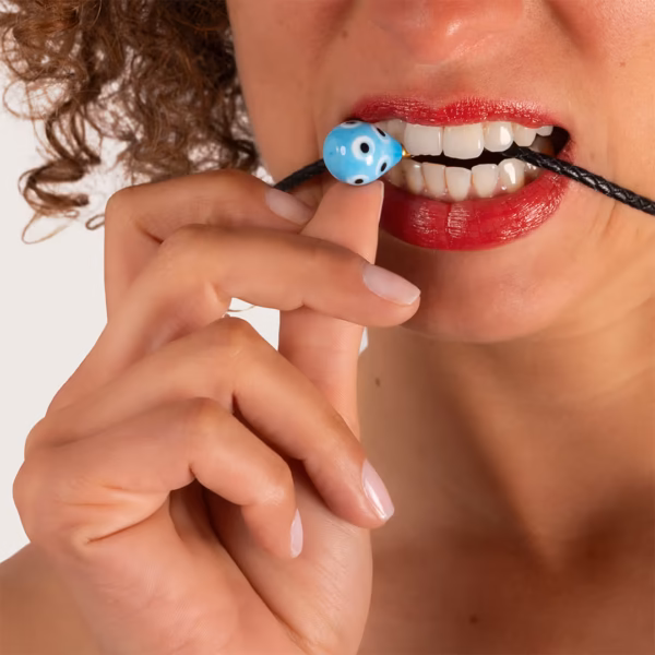 Perle bleue décorative sur collier de cordon cuir noir mordue par une femme brune - Photyne