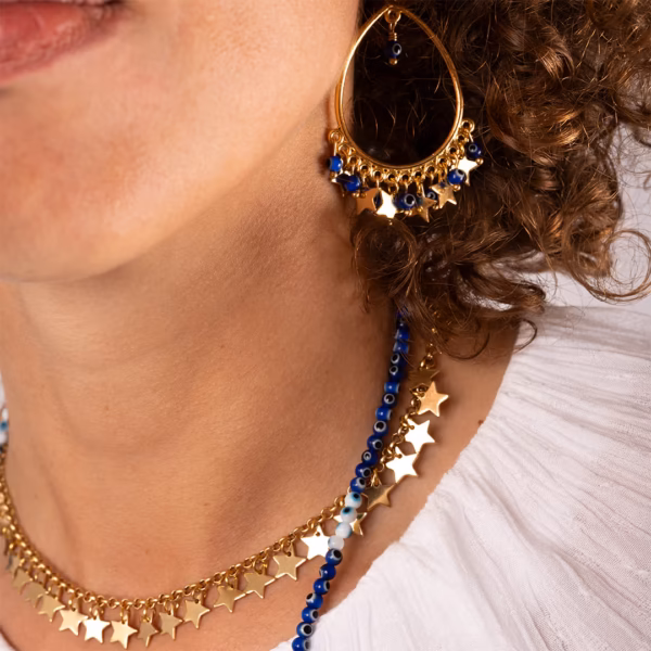 Boucle d'oreille dorée en forme de goutte avec étoiles et perles bleues portée par une femme- Photyne