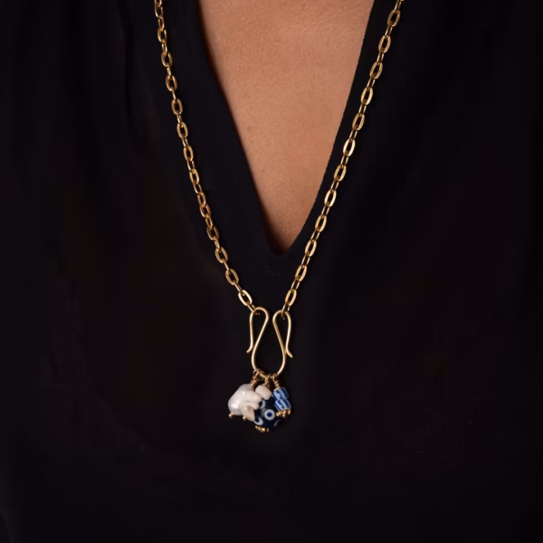 gros plan sur le Collier Eliara par Photyne - longue chaîne dorée avec 4 pendentifs bleus et blancs porté sur un haut noir