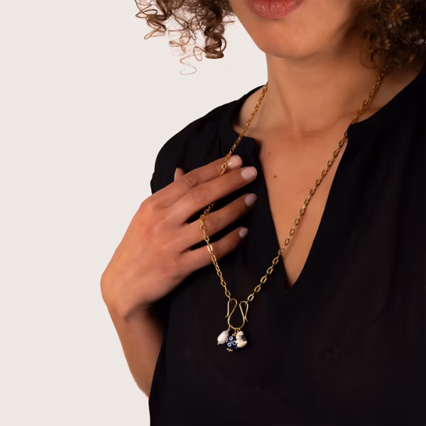 Collier longue chaîne dorée avec pendentifs charms bleu et blanc porté par une femme sur un haut noir- un bijou Photyne