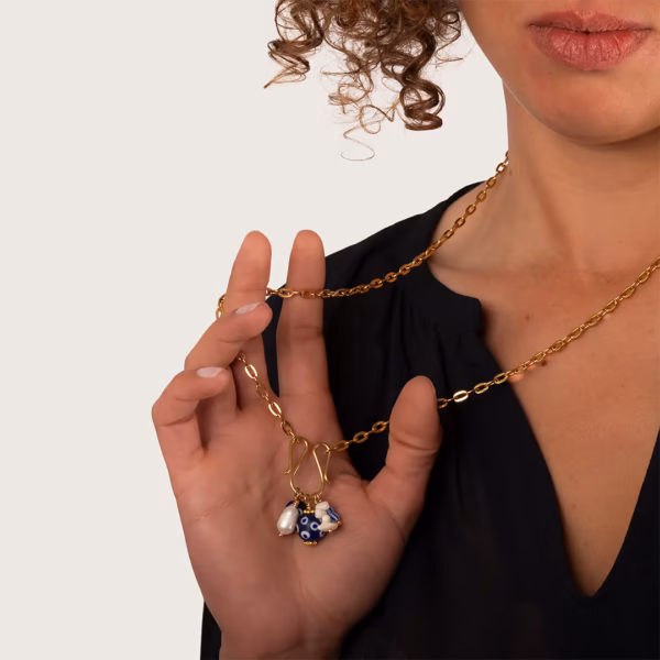 Collier longue chaîne dorée avec pendentifs bleu et blanc porté par une femme sur un haut noir.
