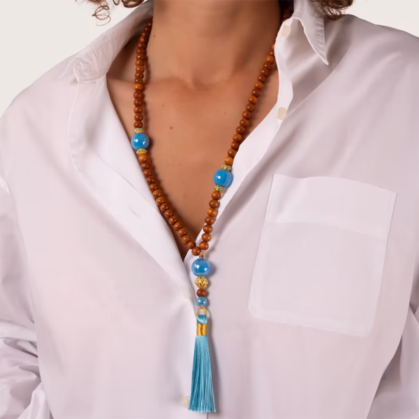 collier de perles de bois de bayong et de perles de céramiques bleues - éléments dorés et pompon turquoise porté par une femme sur une chemise blanche entrouverte