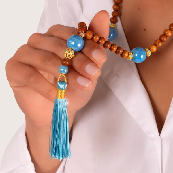 Collier Photyne Mediterranéen en perles bois et bleues avec pompon turquoise porté sur chemise blanche - modèle Nyx