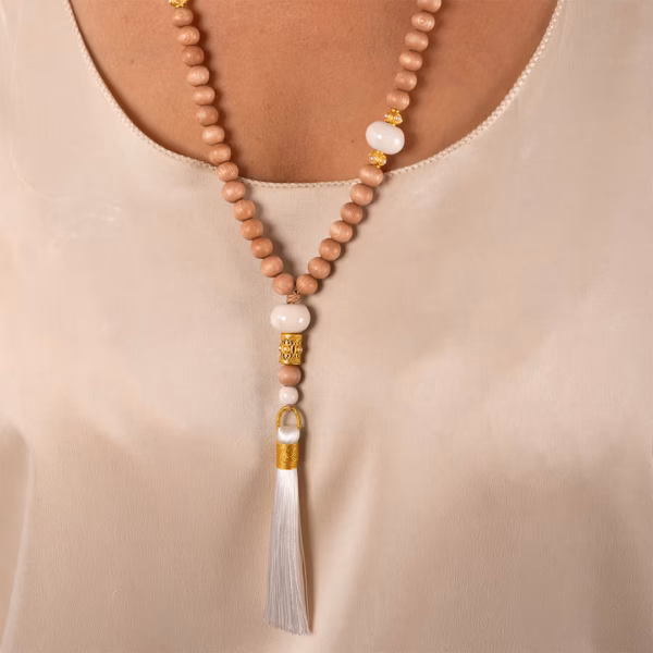 Gros plan sur le Sautoir Chloe par photyne - perles bois et ornements dorés avec pompon blanc porté par une femme.