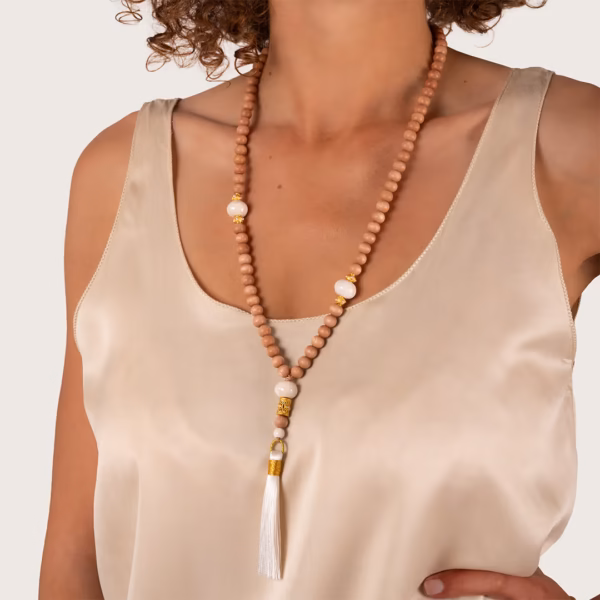 Sautoir Chloe par photyne - perles bois et ornements dorés avec pompon blanc porté par une femme.